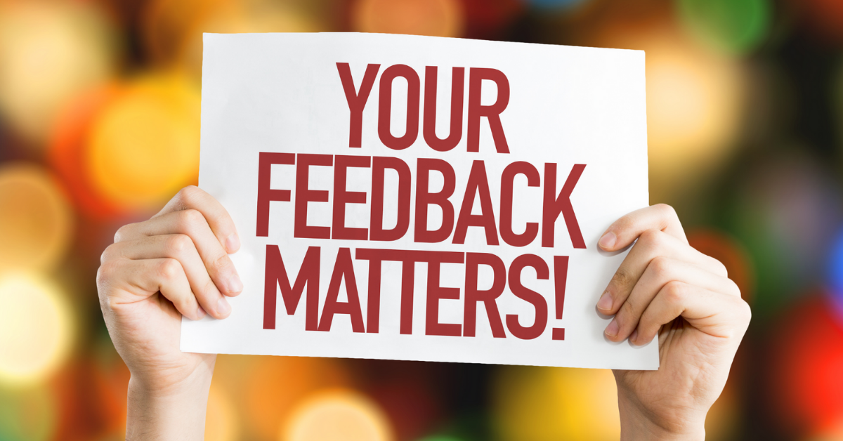  A photo of a person holding a sign that says 'Your feedback matters' in front of a blurred background of bokeh lights.