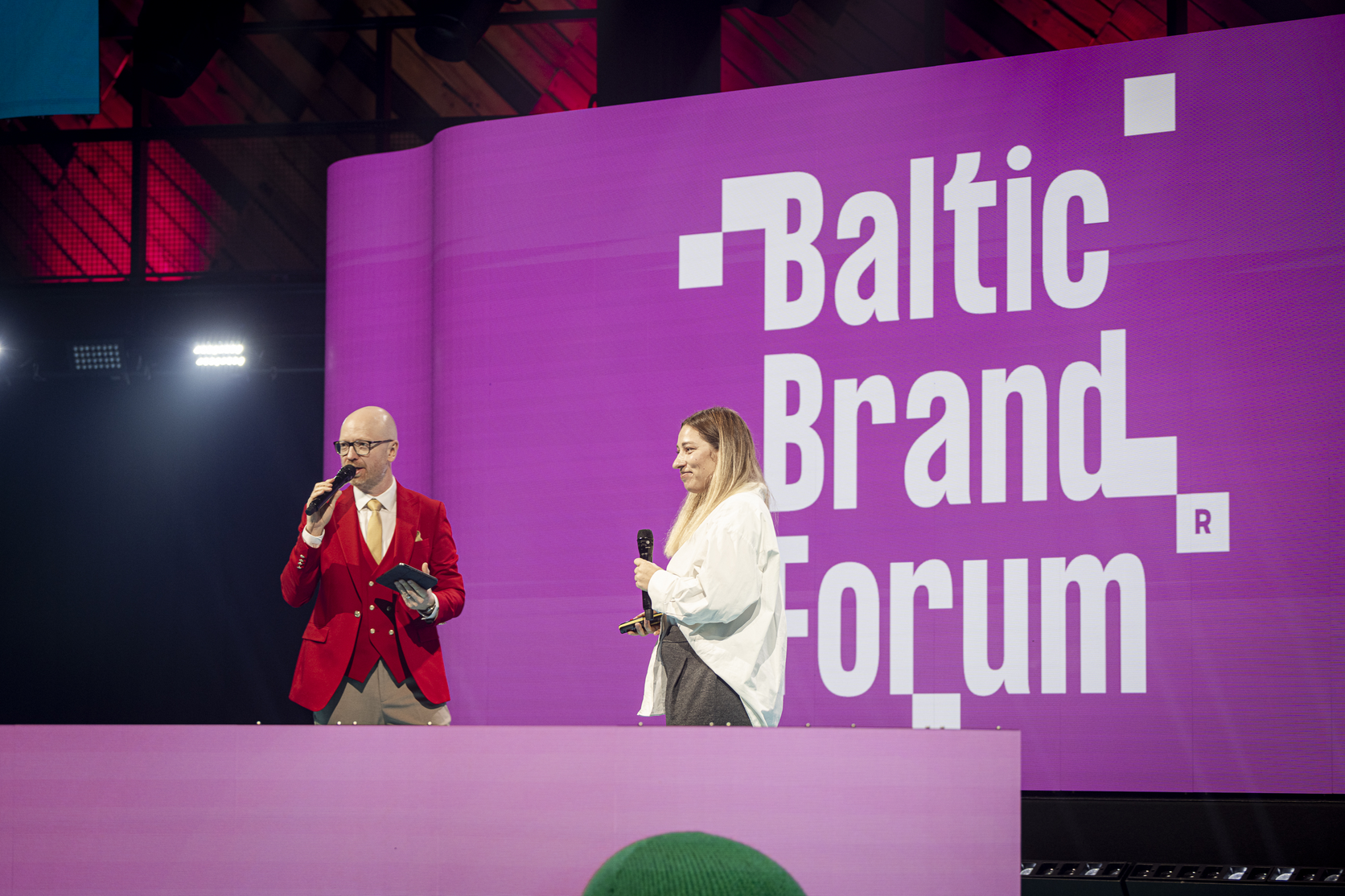 Lina Ivanova and the event host on the Baltic Brand Forum stage in front of the Baltic Brand Forum screen